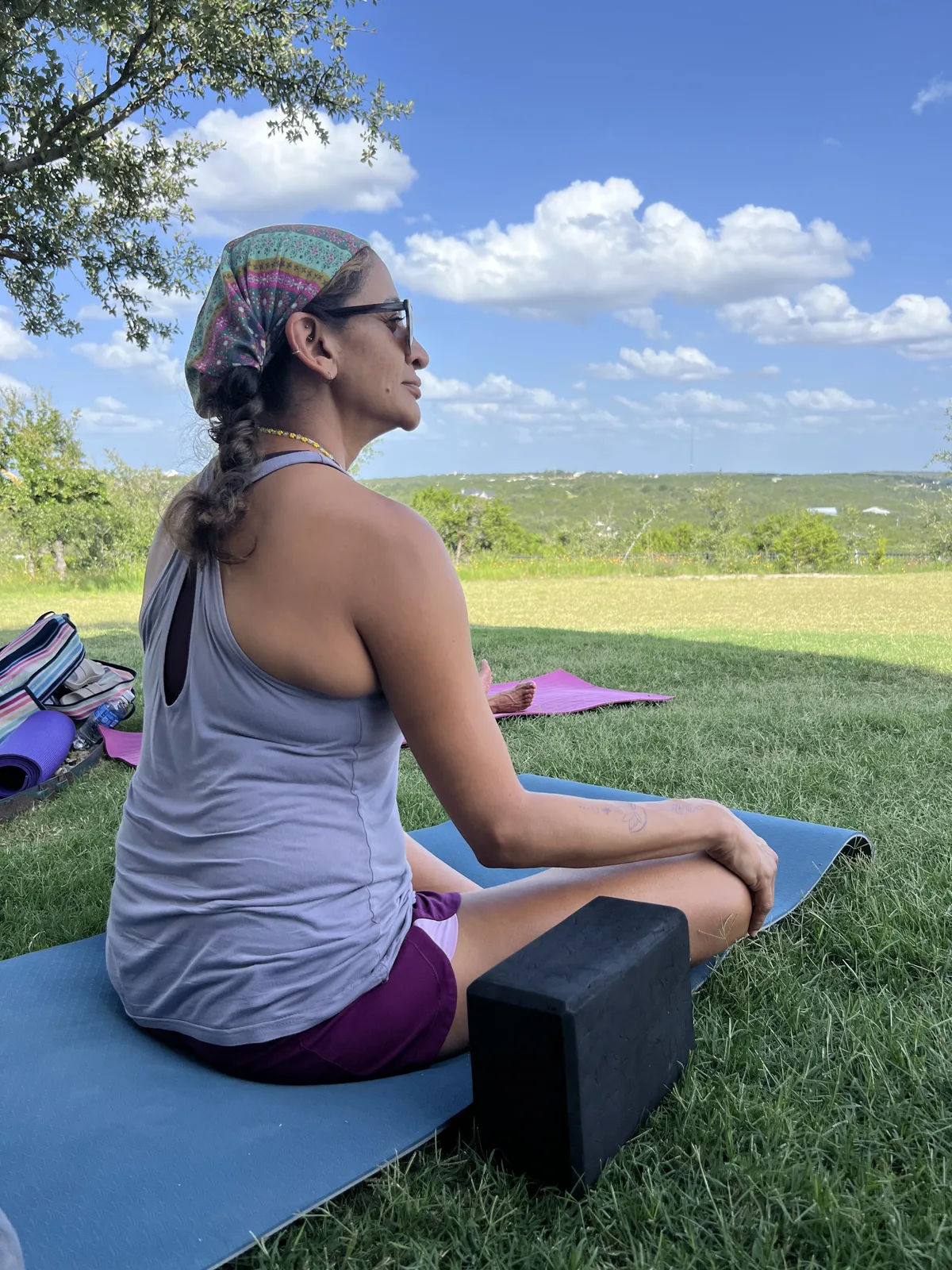 A woman meditating on a yoga mat with the Hill Country stretched out behind her