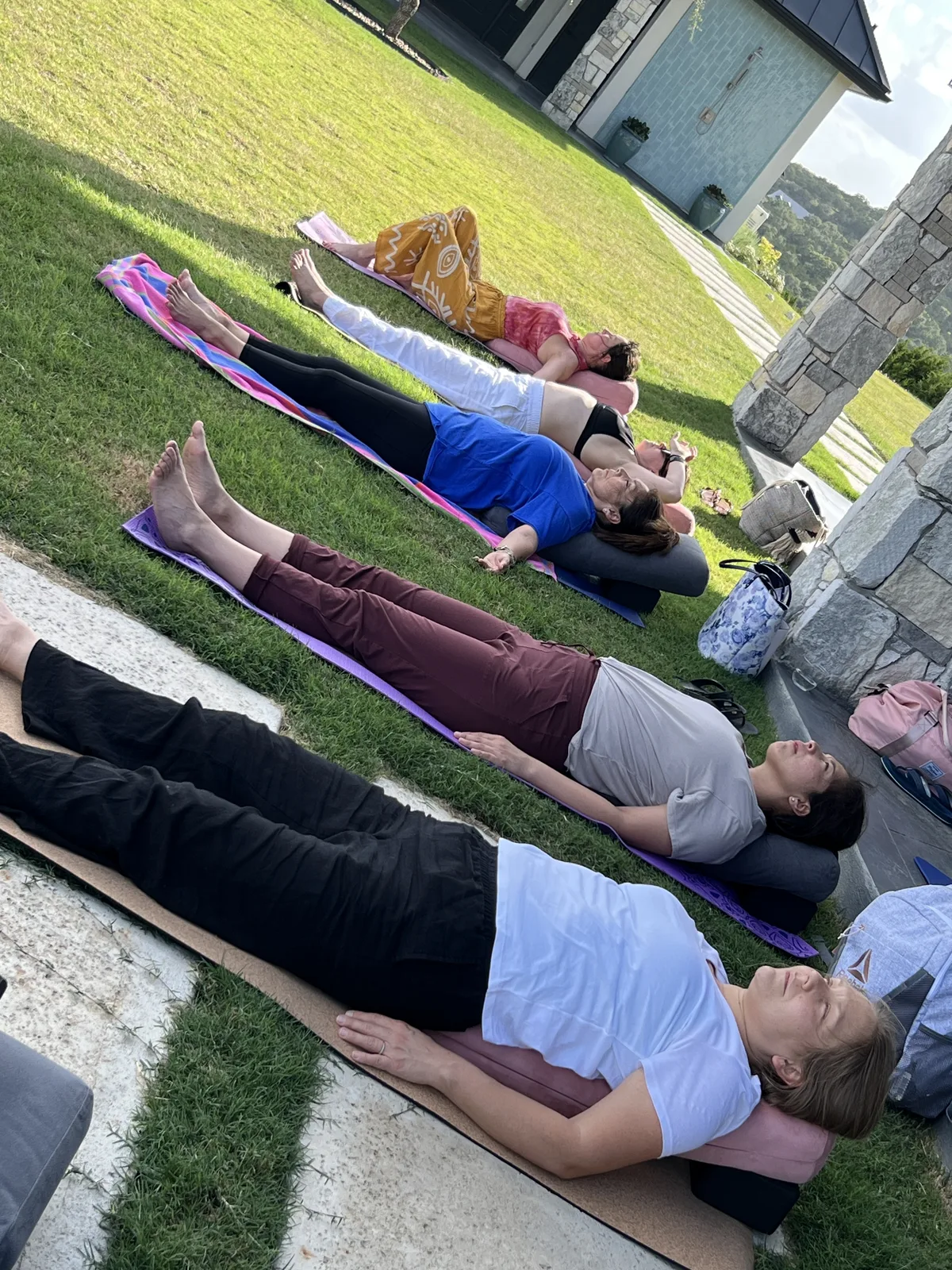 A row of participants resting in savasana on mats in the grass